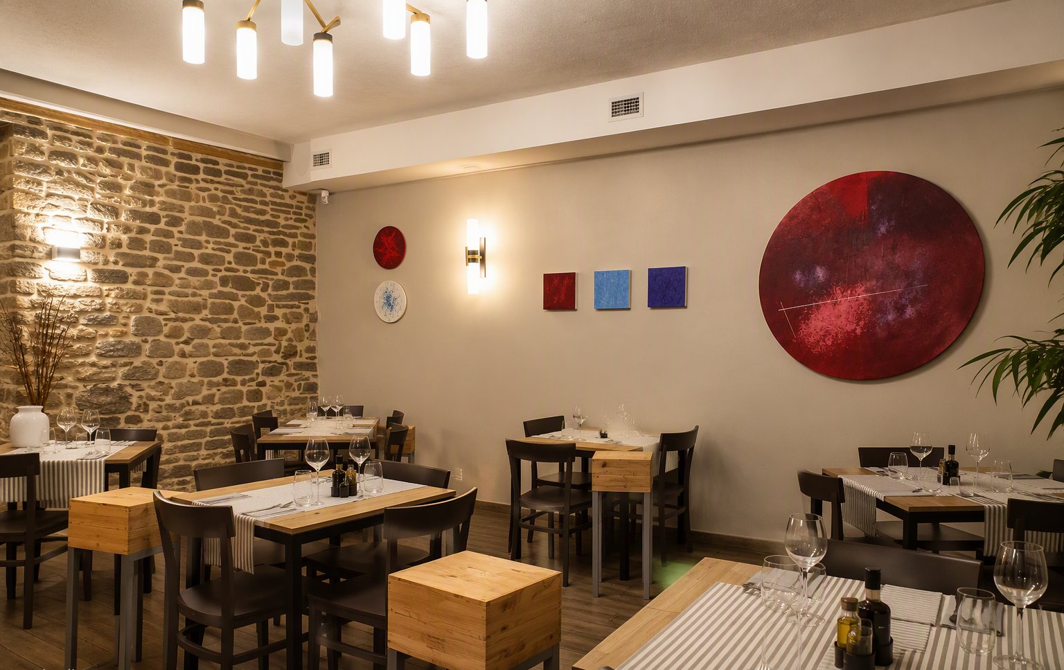 La sala con la parete in pietra, i tavoli apparecchiati e le opere d'arte moderne